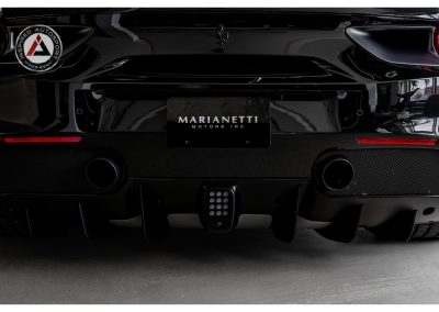 Close-up of sleek black Ferrari sports car rear, showcasing aerodynamic design and dual exhausts, with Inspired Autosport and Marianetti Motors branding.