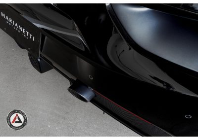 Close-up of sleek black race car rear with carbon fiber accents, showcasing advanced automotive engineering and aerodynamic design for motorsport enthusiasts.