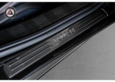 Close-up of Ferrari logo on carbon fiber door sill plate showcasing luxury sports car details and high-performance design.