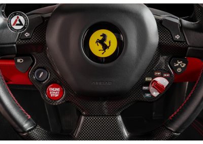 High-quality image of a Ferrari race car steering wheel featuring carbon fiber accents, engine start button, and racing mode selectors for automotive enthusiasts.