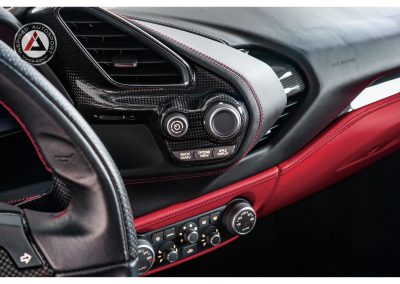 Close-up of luxury sports car dashboard with carbon fiber accents, air vents, and advanced control dials, highlighting precision engineering and premium design elements.