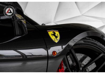 Close-up of a black Ferrari race car showing the iconic Ferrari shield emblem and details of the wheel, emphasizing high-performance luxury vehicles at Inspired Autosport.