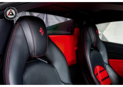 Close-up of luxury black leather Ferrari racing seats with red stitching and embroidered prancing horse logo, inside a high-performance sports car.