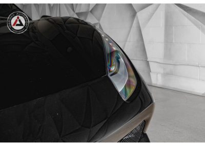 Close-up of a sleek, black sports car headlight with a modern design, highlighting advanced automotive lighting technology in a stylish showroom setting.