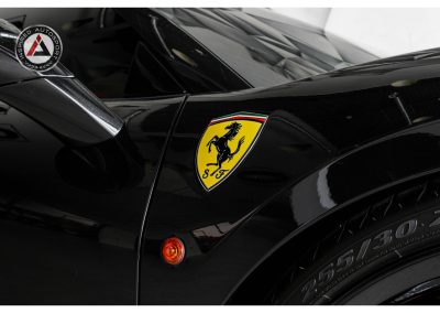 Close-up of Ferrari emblem on high-performance black vehicle, showcasing luxury and speed with detailed Ferrari badge and tire detail.
