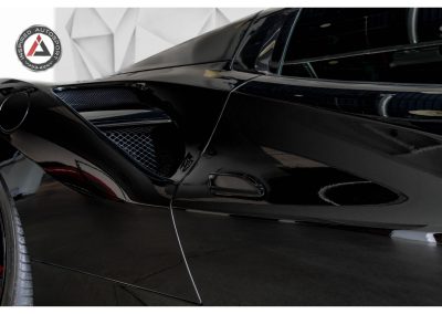 Close-up of sleek black supercar with aerodynamic design, carbon fiber accents, and racing-inspired styling showcasing automotive excellence.