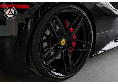 Close-up of a black Ferrari wheel with red brake calipers, highlighting high-performance tires and custom rims for luxury sports car enthusiasts.