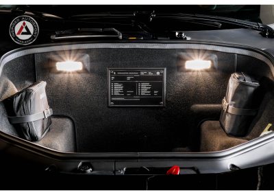 Close-up of a race car trunk with organized storage bags, interior lighting, and a personalized information display, showcasing automotive customization and racing readiness.